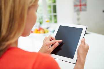 Woman Using Digital Tablet At Home In Kitchen