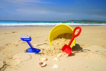 Child's beach bucket and spade on a sandy beach with seashells © Leah-Anne Thompson