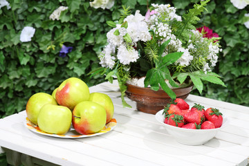 Plates with apples, strawberries and flowers on white table.