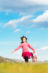 Happy little schoolgirl with bag running on fied