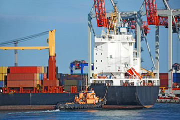 Tugboat assisting container cargo ship to harbor quayside
