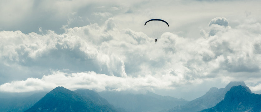 Paraglider over mountains and cloudy sky background