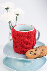 Blue cup with red knitted cover and cookies with chocolate