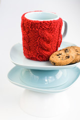 Blue cup with red knitted cover and cookies with chocolate