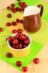 Ripe red cherry berries in bowl on wooden table close-up