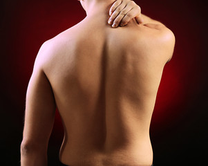 Young man with neck pain, on red background