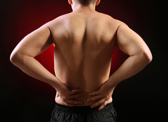 Young man with back pain, on red background
