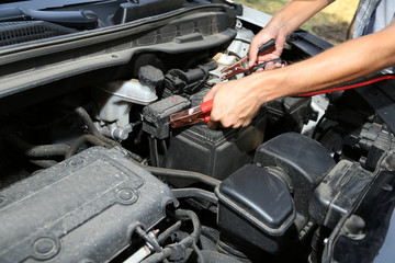 Car mechanic uses battery jumper cables to charge dead battery