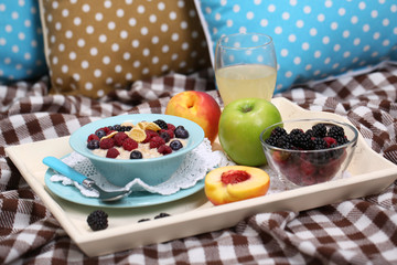 Oatmeal in plate with berries on napkins on wooden tray on bad