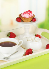 Cup of tea with cakes on wooden tray on table in room