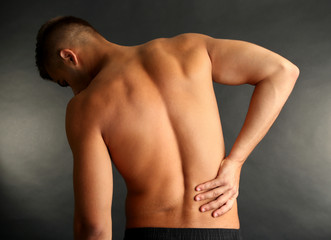 Young man with back pain on grey background