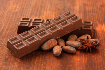 Delicious chocolate bars with cocoa beans on wooden background
