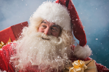 Photo of happy Santa Claus outdoors in snowfall carrying gifts t