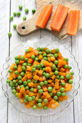 Boiled carrots with green peas in glass bowl