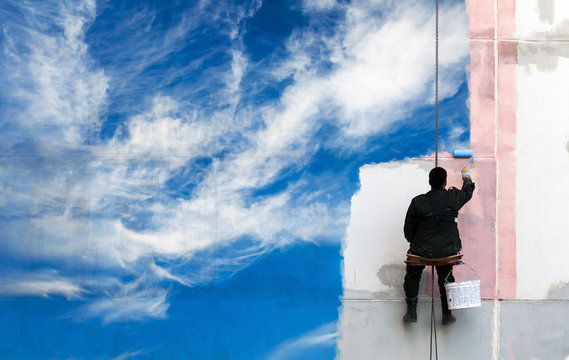 Painter paints bright blue sky on the urban wall