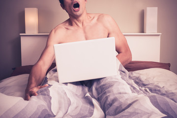 Young man is sitting in bed and watching pornography on laptop