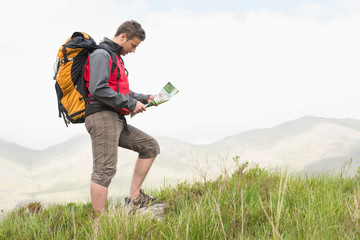 Handsome hiker with backpack hiking uphill reading a map