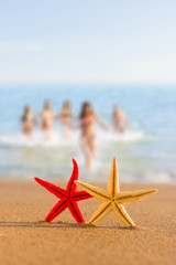 Fototapeta na wymiar starfish on the beach at sunrise with girls on BG