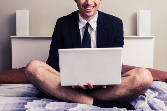 Young businessman with laptop sitting on bed in his underwear