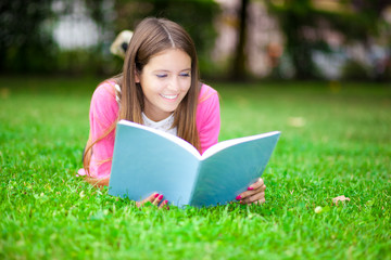 Fototapeta premium Young female student reading a book on the grass