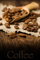 Coffee beans in a wooden scoop on wooden background