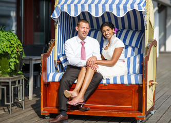 Beautiful indian bride and caucasian groom, in beach chair.