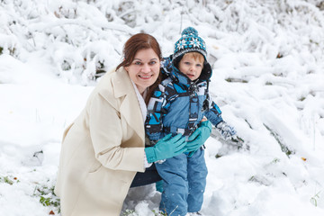 Fototapeta na wymiar Young woman and her little son having fun with snow in winter fo