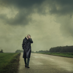 grim man in a black cloak walking on the road alone