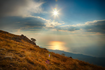 Hillside, sea and sky with clouds and sun