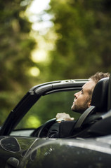 Elegant young happy man in convertible car outdoor.