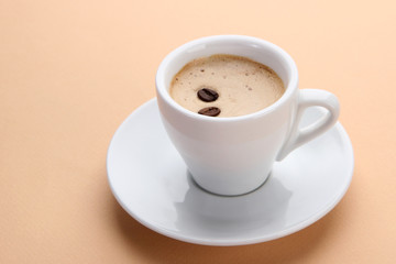 Cup of coffee with coffee beans on beige background