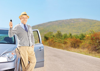 Smiling senior male holding a key next to his automobile