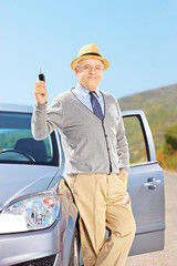 Smiling senior male holding a key next to his automobile outside