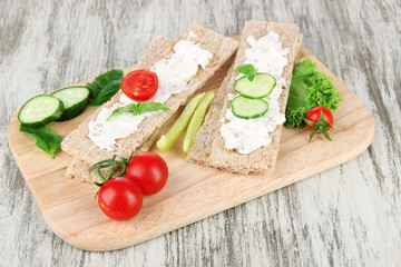 Tasty crispbreads with vegetables on wooden background