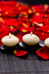 Set of stones with candle on mat with red rose petals