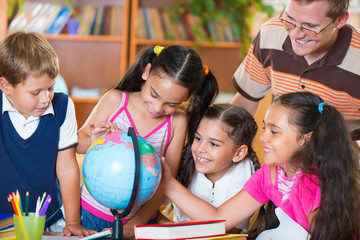Portrait of pupils looking at globe with their teacher