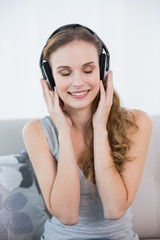 Naklejka premium Content young woman sitting on sofa listening to music