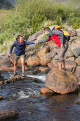 Man helping his girlfriend to cross a river