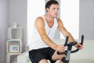 Fototapeta na wymiar Attractive sporty man exercising on bike and listening to music