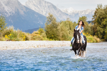 Smiling Female horse rider crossing river in a mountainous lands