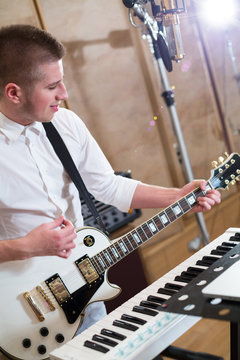 Guitarist playing guitar next to keyboards in studio