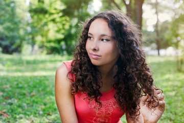 Smiling teenage girl with curly hair sitting on a green grass