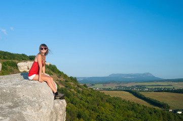 Naklejka na ściany i meble Smiling young woman sitting on the edge of mountain