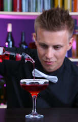 Portrait of handsome barman preparing cocktail, at bar