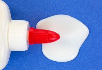 Close view of spilled white glue and bottle on blue paper