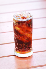 glass of cola with ice with wood background