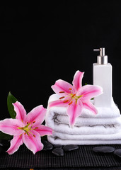 Fototapeta na wymiar Lily pink flower on towel and spa oil on pebbles