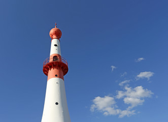 Red and white lighthouse against blue sky