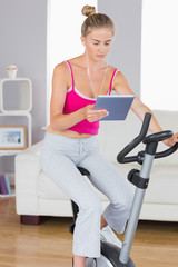 Fototapeta na wymiar Sporty serious blonde training on exercise bike using tablet