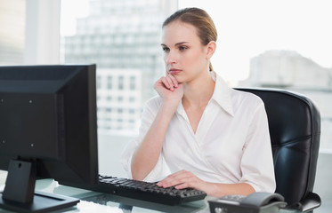 Thoughtful businesswoman sitting at desk looking at computer